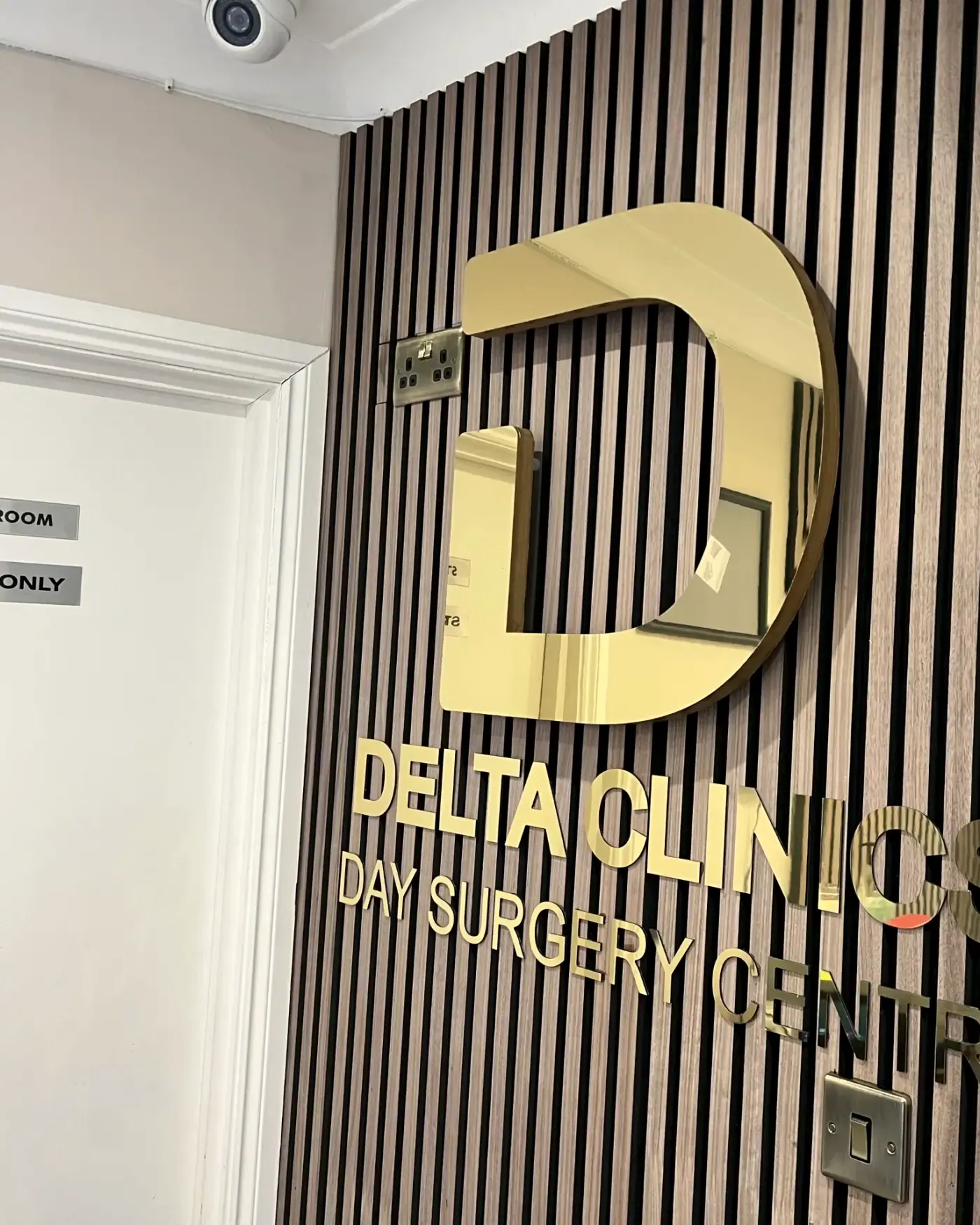 Gold mirror logo and letters on a timber slat wall at Delta Clinics