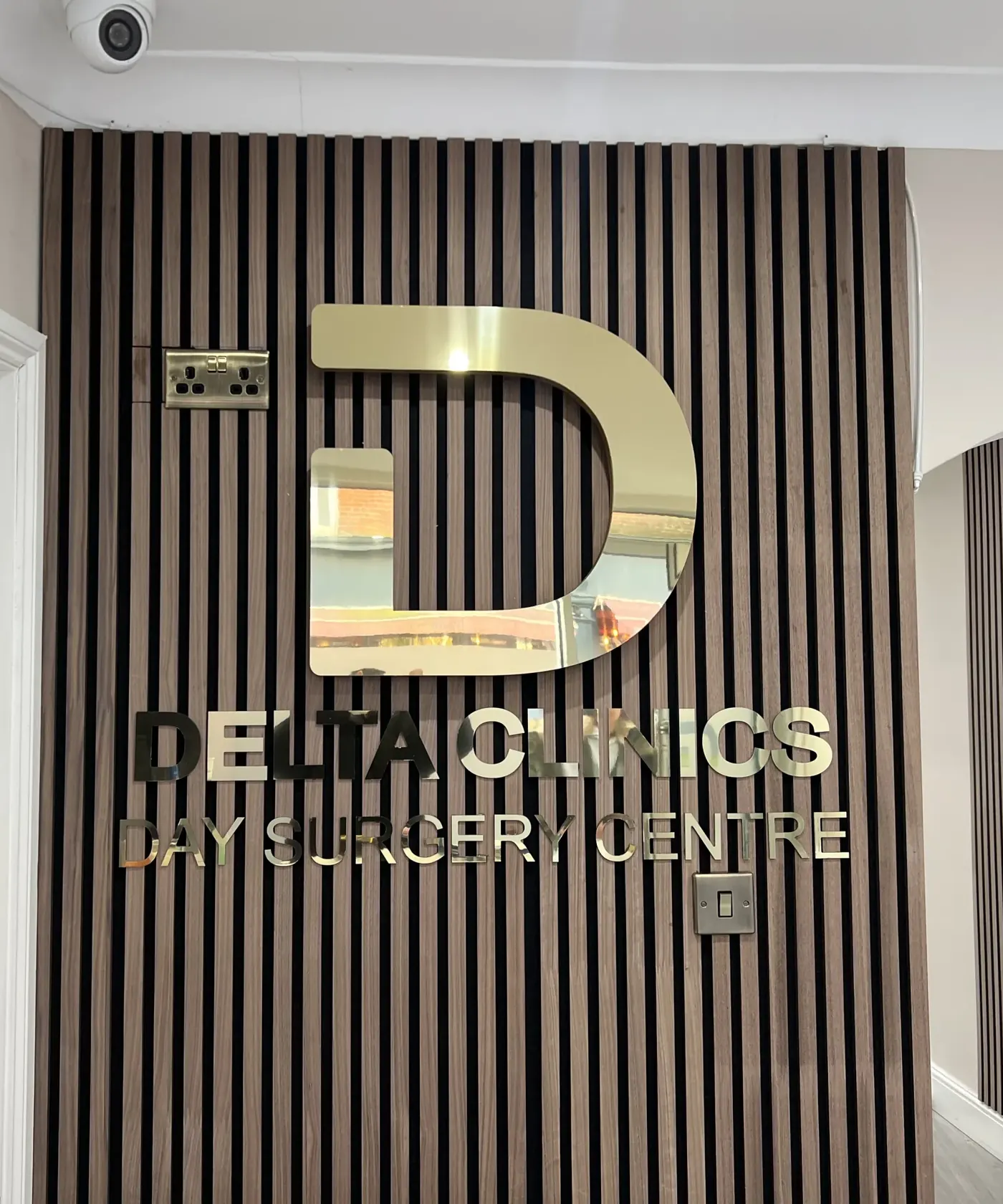 Gold mirror logo and letters on a timber slat wall at Delta Clinics