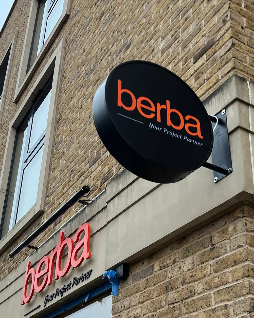 Round black projecting sign with the Berba logo in orange on a wall bracket, Twickenham