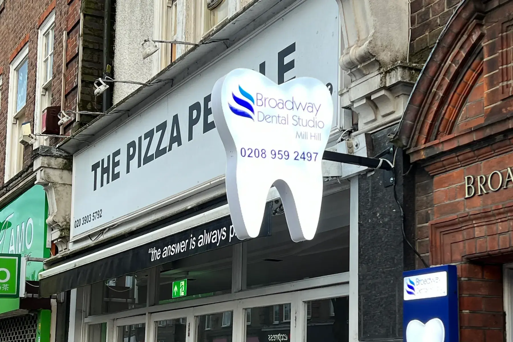 Broadway Dental Studio's white tooth-shaped projecting sign on its bracket above the high street in Mill Hill
