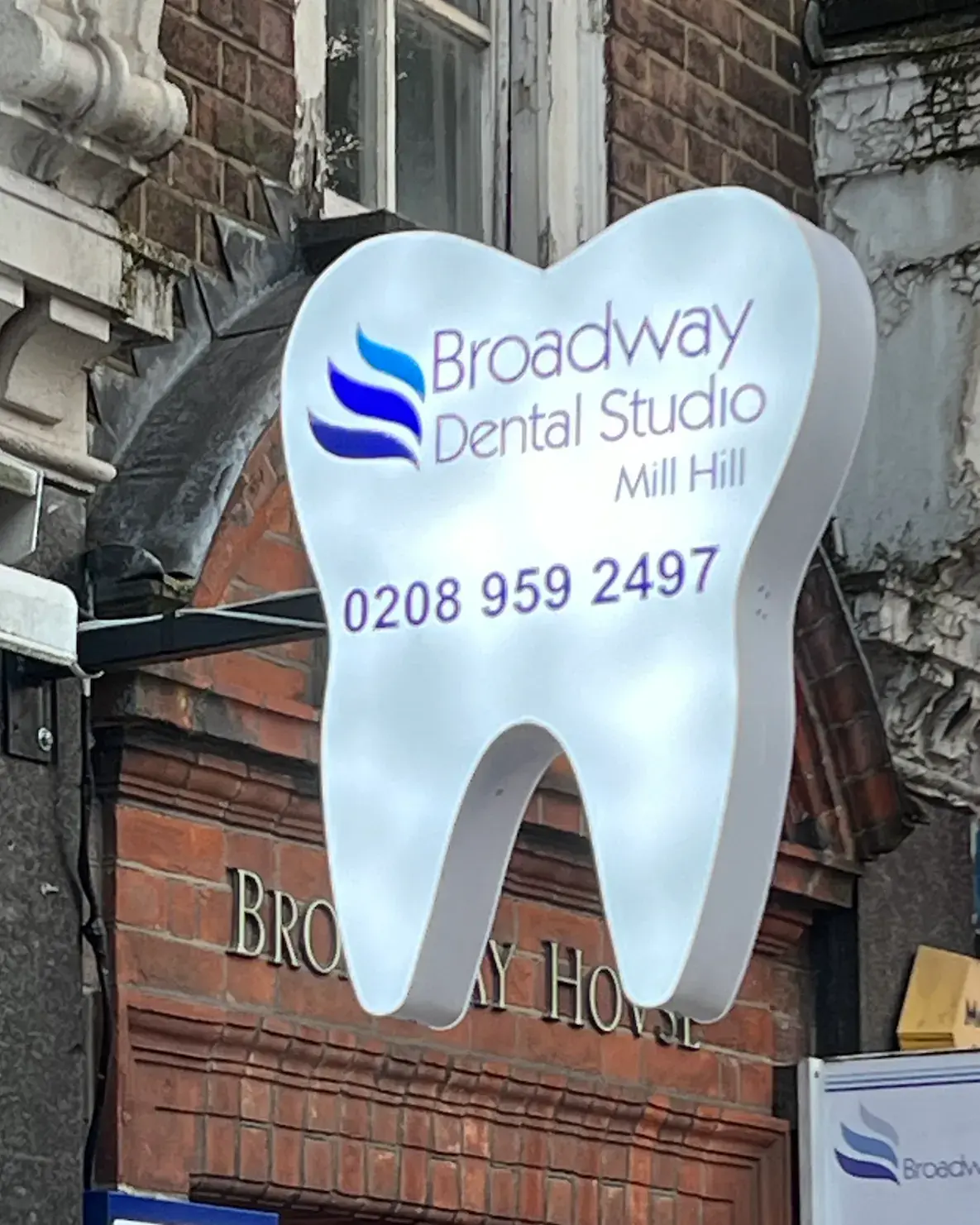 Tooth-shaped projecting sign for Broadway Dental Studio, Mill Hill, with the practice name and phone number on its face
