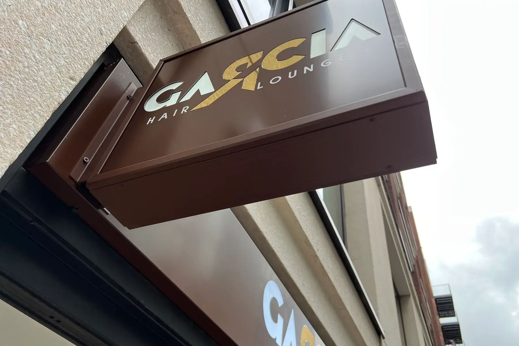 Garcia Hair Lounge projecting sign seen from below, with the matching fascia sign underneath