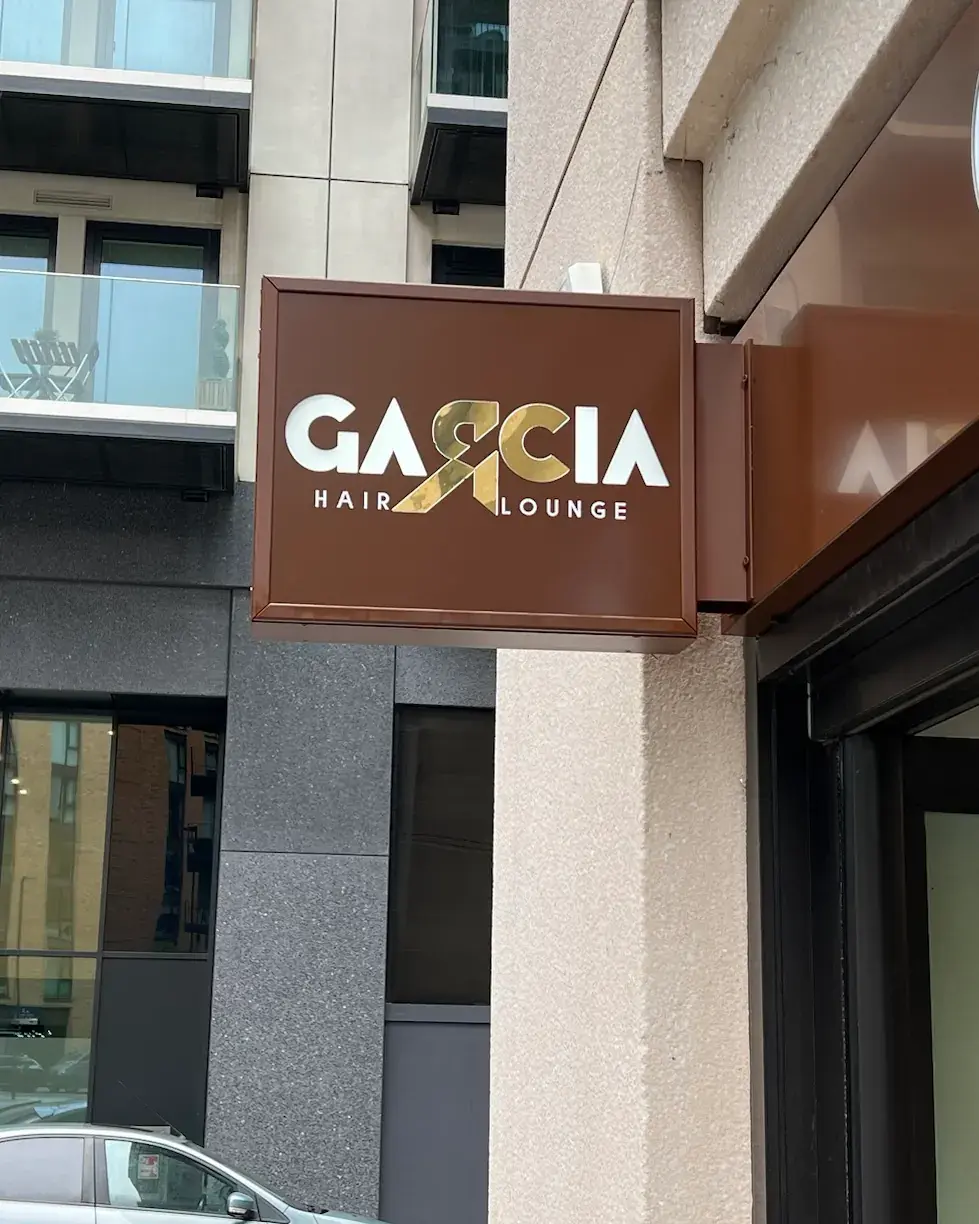 Brown projecting box sign with the Garcia Hair Lounge logo in white and gold
