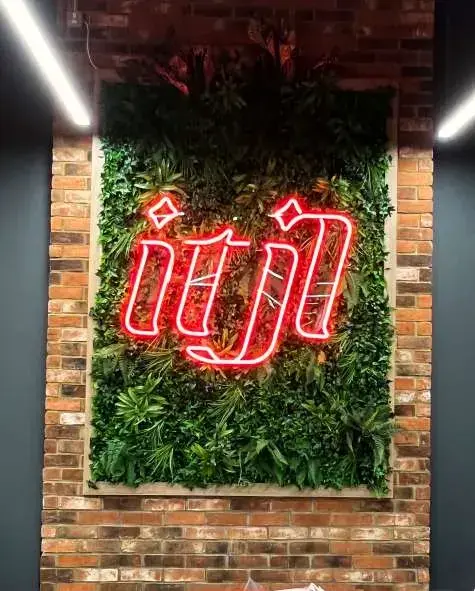Red neon ITJL sign on a moss wall set in exposed brick, inside the restaurant in Colindale