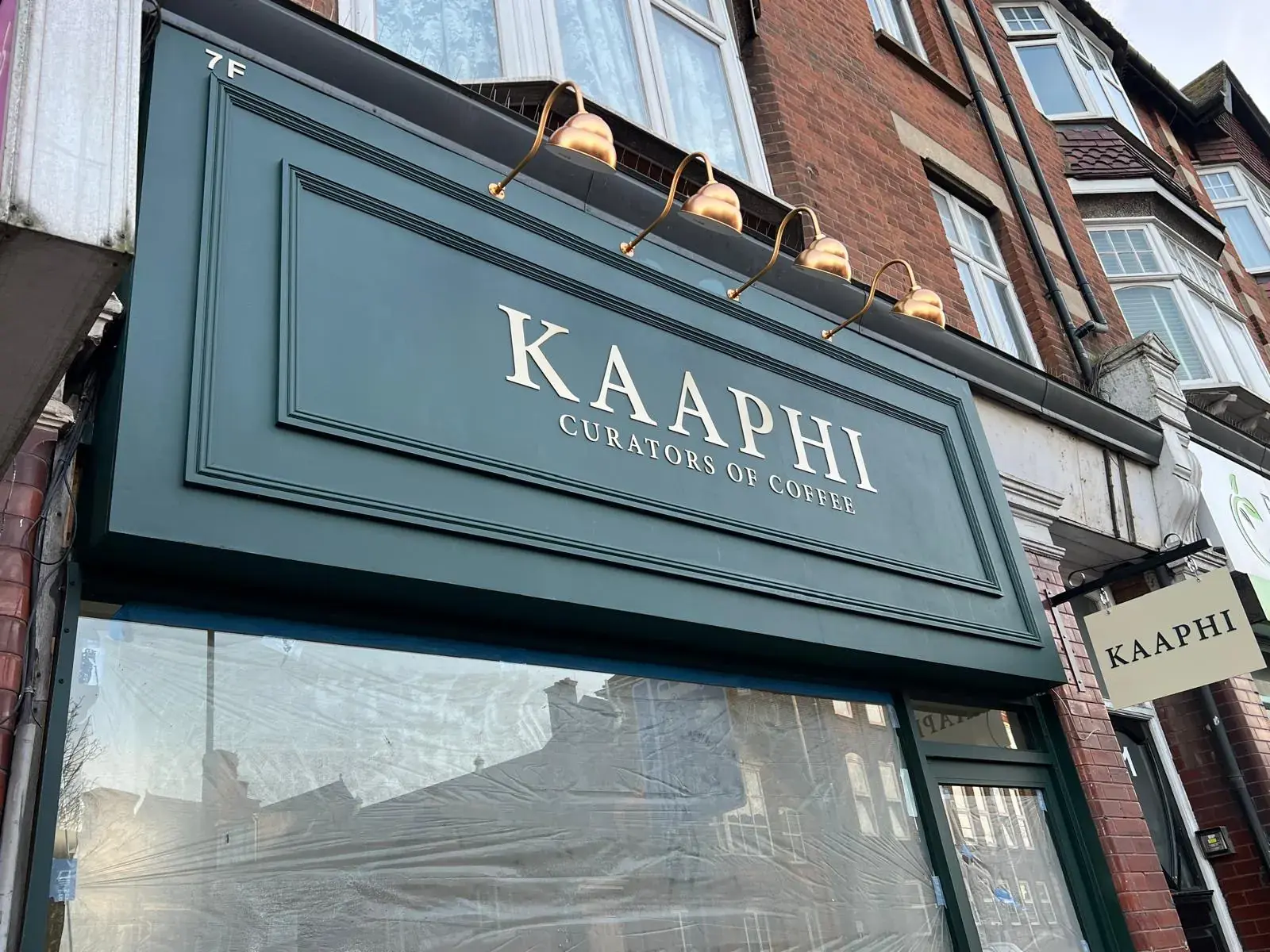 The Kaaphi fascia seen at an angle, with the cream hanging sign on its black bracket to the right