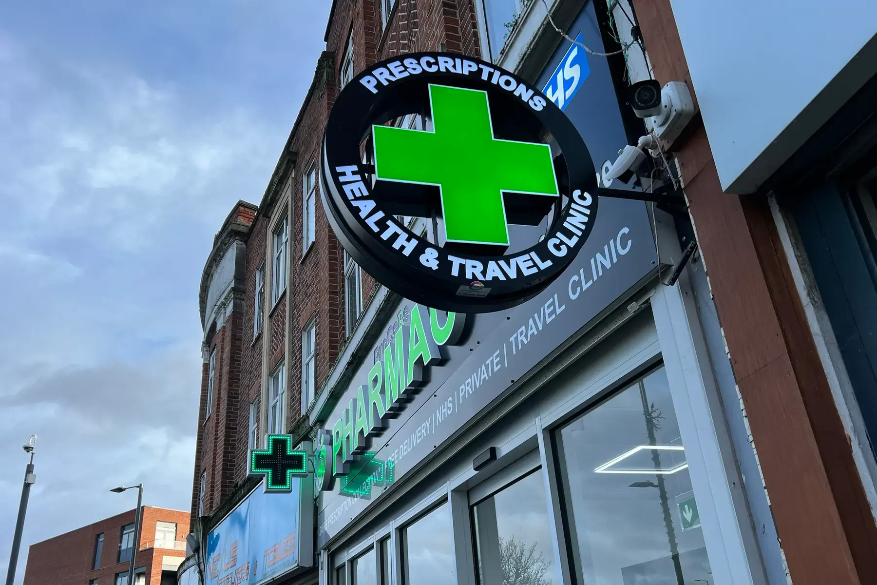 Round projecting sign with an illuminated green cross on its wall bracket at ProCare Pharmacy