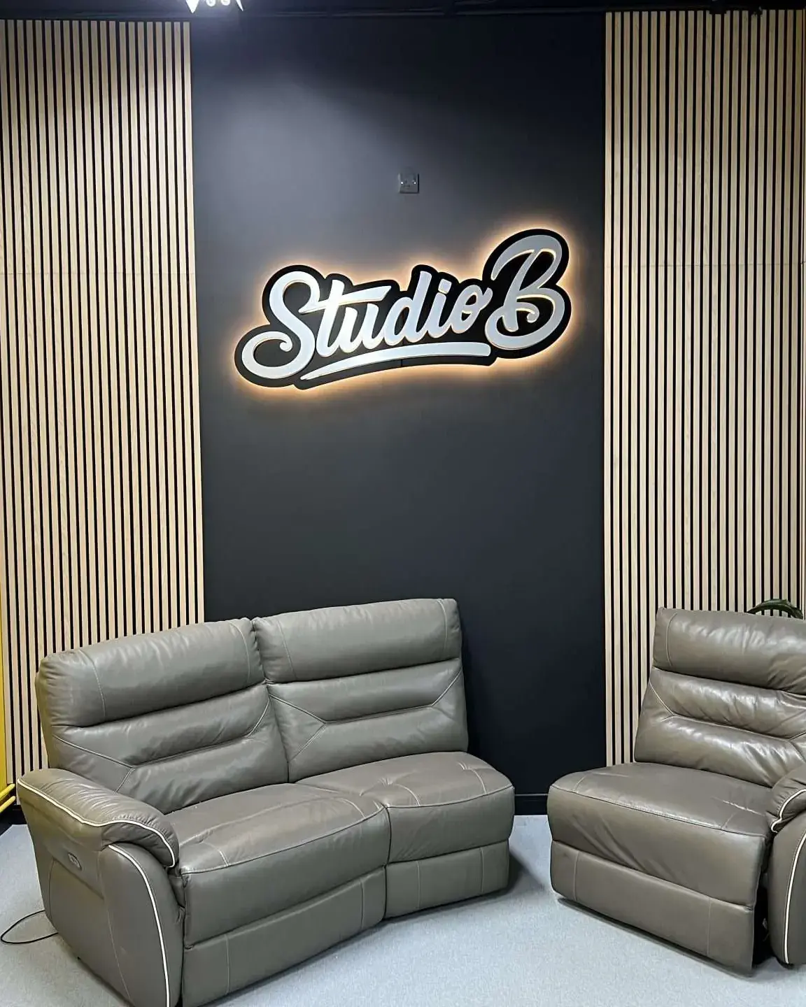 Halo-lit Studio B sign on a dark wall between timber slats, above the reception sofas