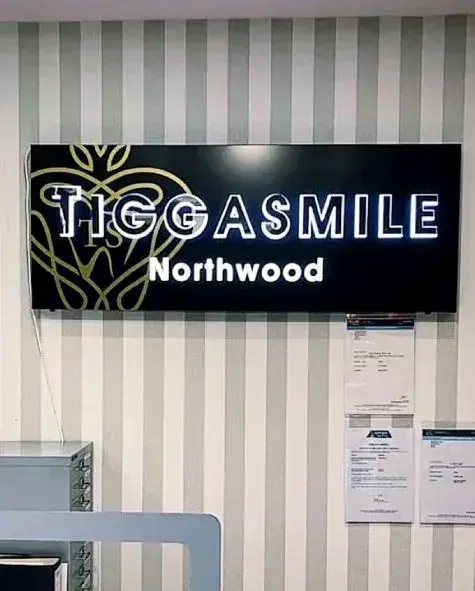 Black TiggaSmile Northwood sign with a gold emblem on a striped wall inside the clinic