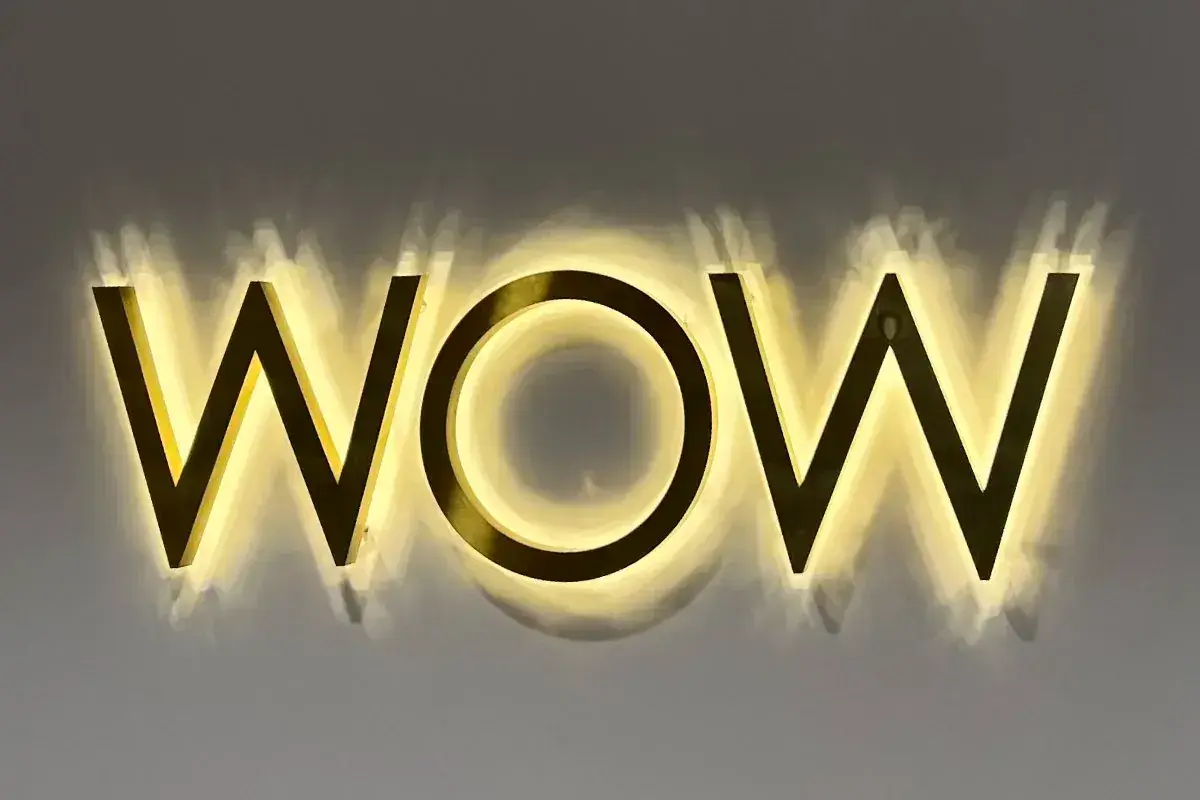 Gold WOW letters with a warm halo on a grey wall inside the salon