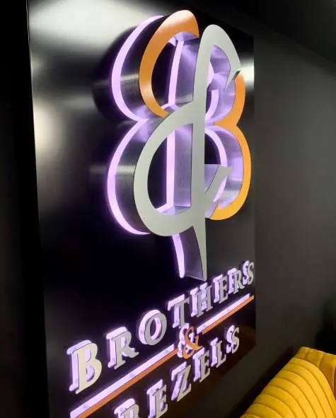 Brothers & Bezels 3D logo and letters with a violet halo on a black wall