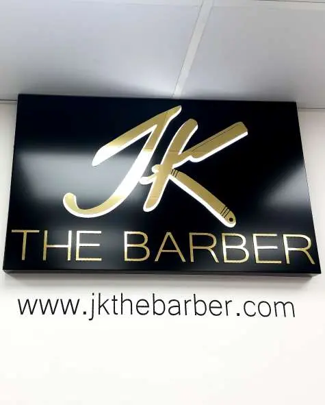 Black panel with gold mirror JK The Barber letters on a white wall