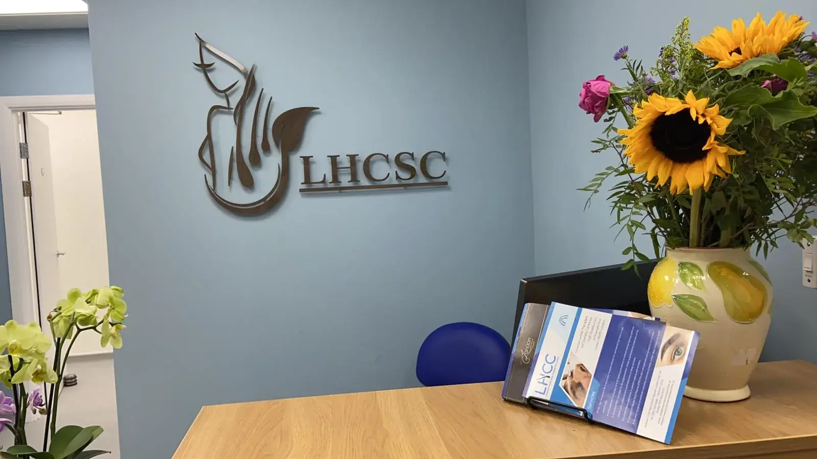 Raised LHCSC logo and letters on a pale blue wall behind a reception desk