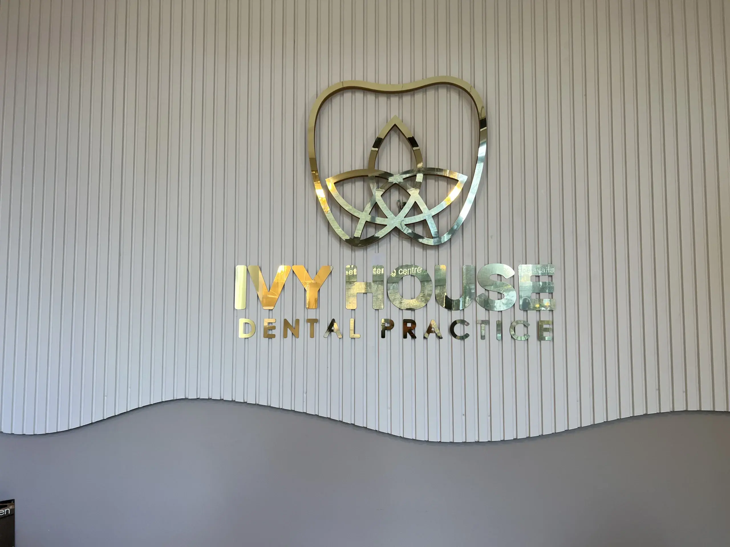 Gold mirror Ivy House Dental Practice logo and letters on a fluted white wall