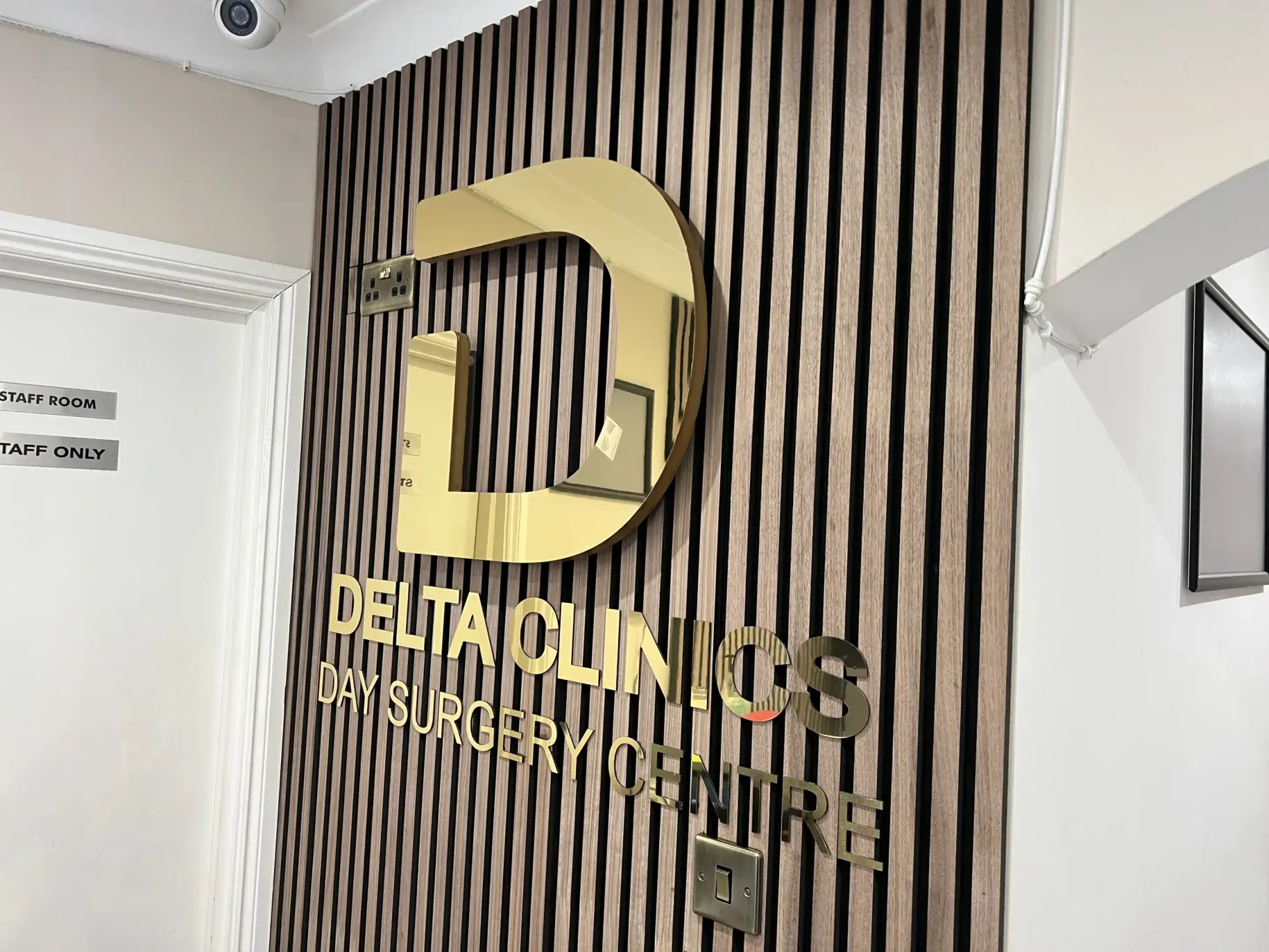 Gold mirror D logo and Delta Clinics Day Surgery Centre letters on a timber slat wall
